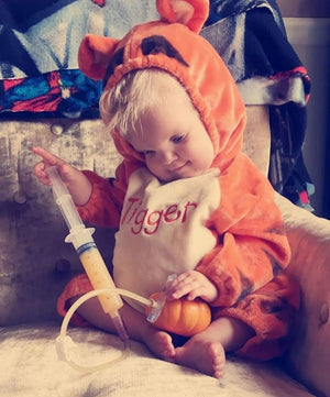 Image shows WB in a 'Tigger' custome from Winnie the Pooh, he is olding a pumpkin with a feedtube tube button, and a syringe filled with nutrition!